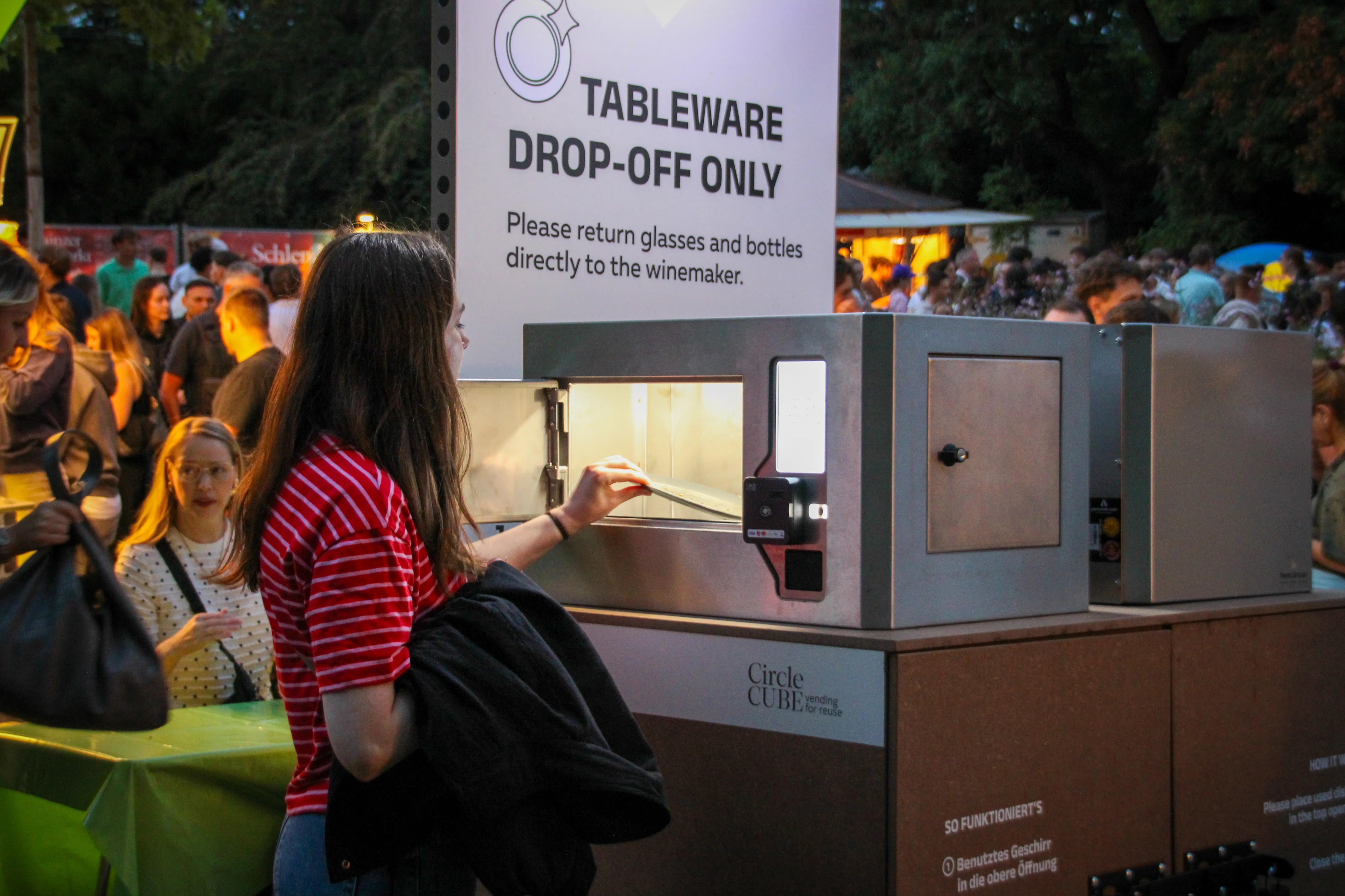 Foto einer Frau auf einem Festival, die einen Teller in eine Box legt, über der Box ein Schild mit dem Schriftzug "Tableware-drop off only"